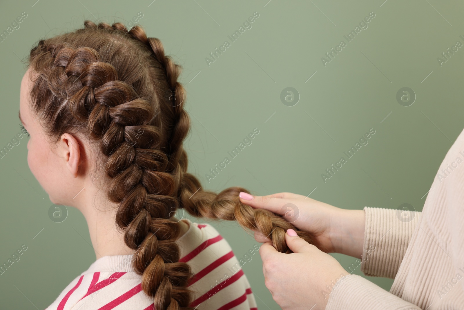 Photo of Professional stylist braiding woman's hair on olive background, closeup