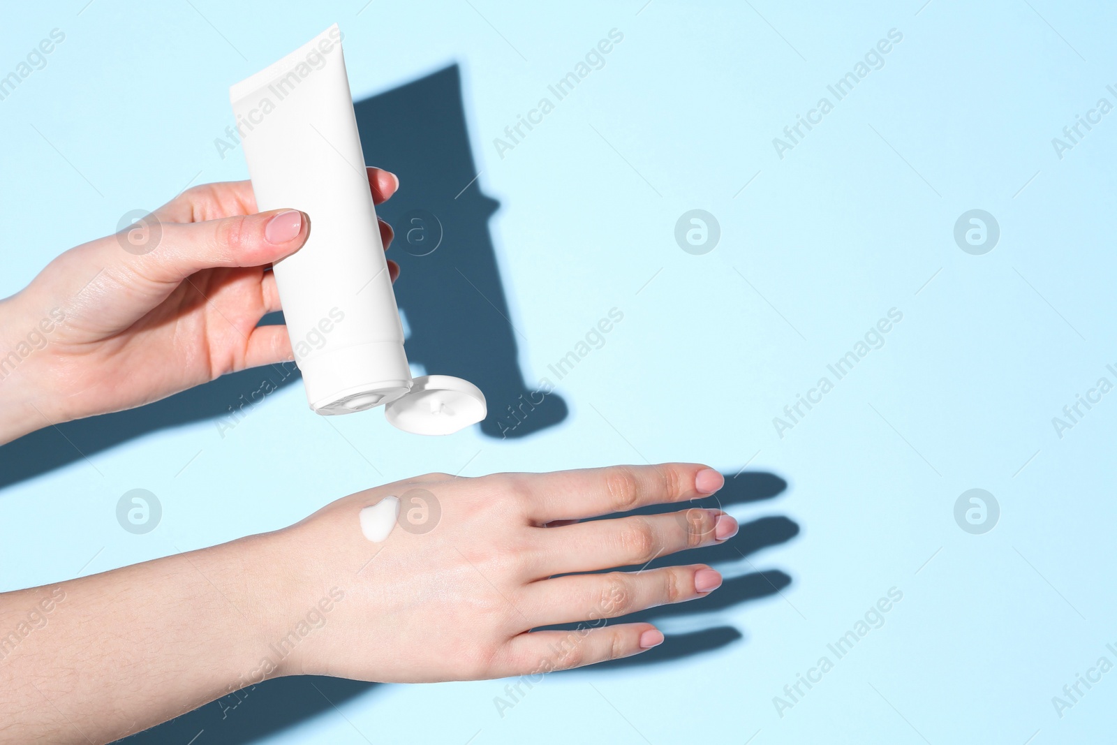 Photo of Woman with tube applying cream on her hand against light blue background, closeup. Space for text