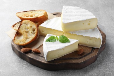 Photo of Tasty brie cheese with basil, bread and almonds on grey table
