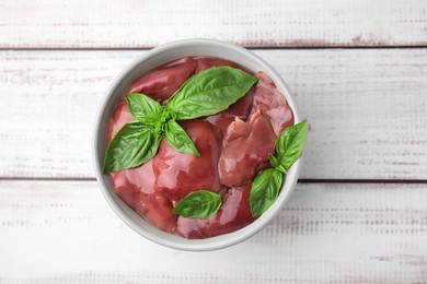 Photo of Bowl with raw chicken liver and basil on white wooden table, top view