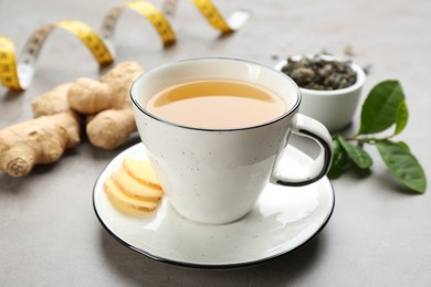 Cup of herbal diet tea, ginger and measuring tape on light table