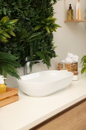 Green artificial plants, vessel sink and different personal care products in bathroom