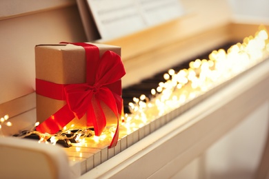 Photo of Gift box and fairy lights on piano keys, space for text. Christmas music