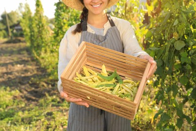 Photo of Young woman holding wooden crate with fresh green beans in garden, closeup