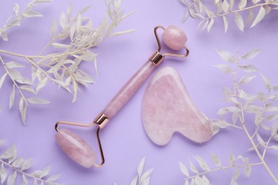 Photo of Gua sha stone, face roller and dry white leaves on violet background, flat lay