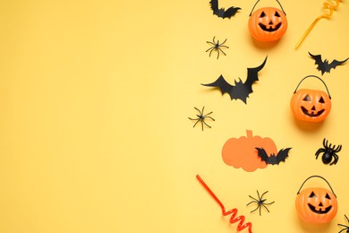 Photo of Flat lay composition with paper bats, plastic pumpkin baskets, spiders and cocktail straws on yellow background, space for text. Halloween decor