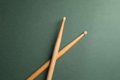 Photo of Two wooden drum sticks on olive background, top view