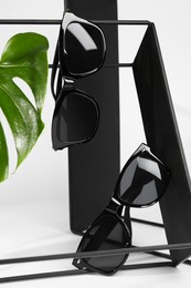 Photo of Stylish sunglasses hanging on black shelf against white background