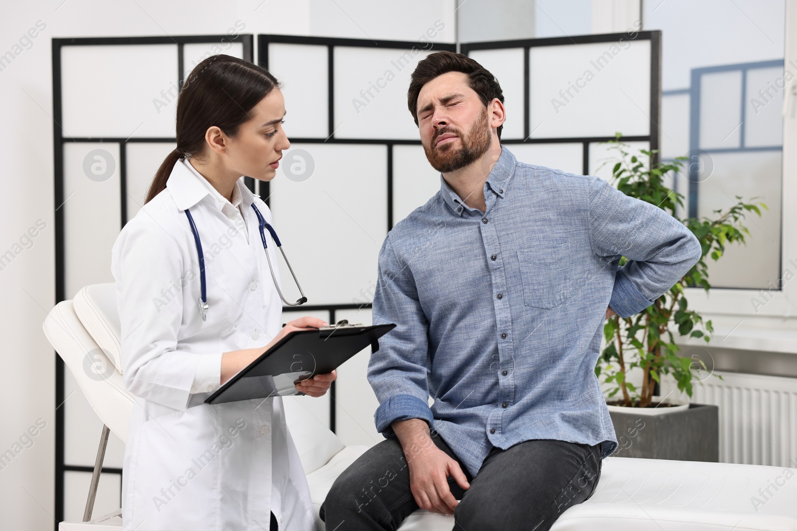 Photo of Doctor with clipboard consulting patient during appointment in clinic