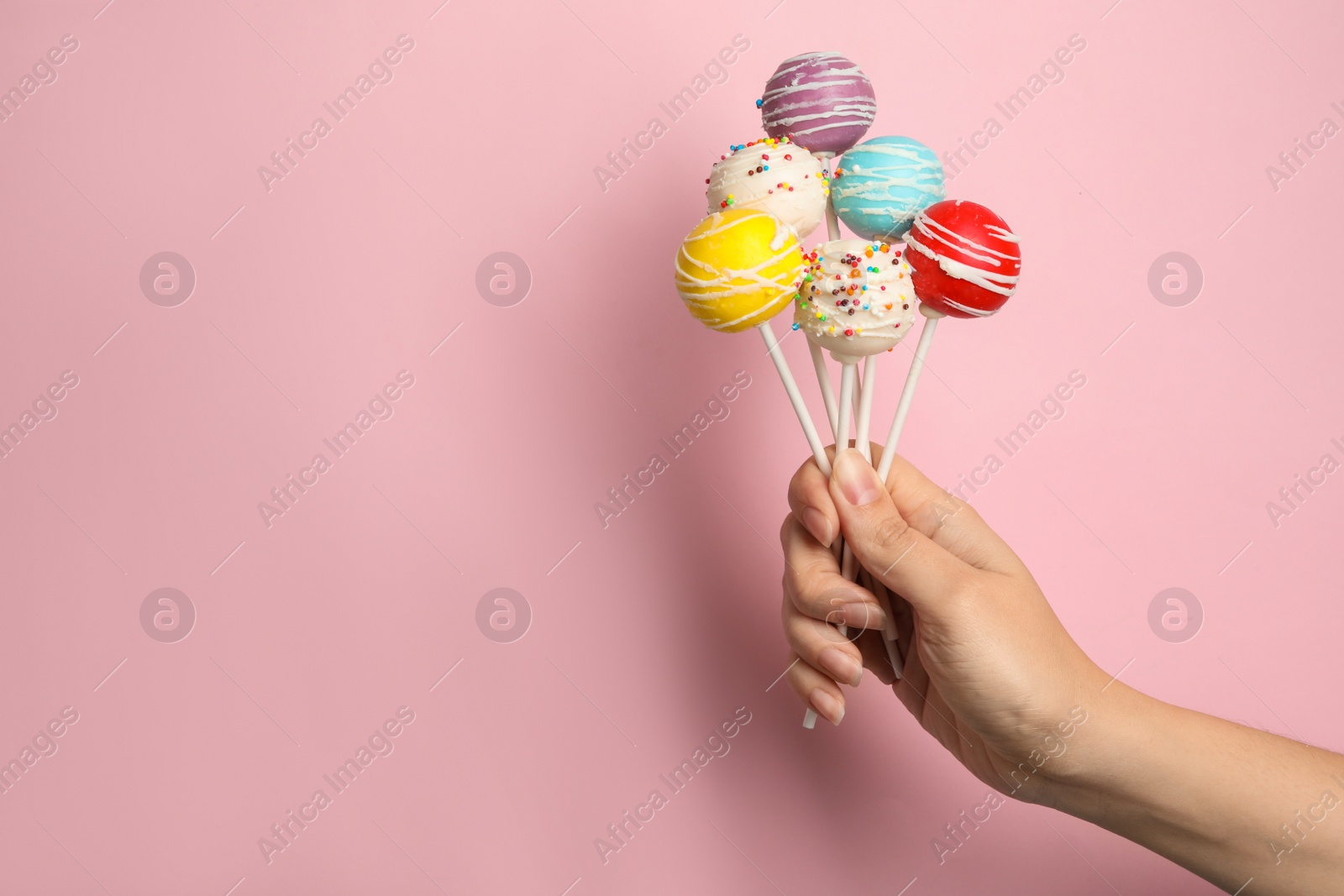 Photo of Woman holding bright delicious cake pops on color background, closeup. Space for text