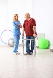 Photo of Caretaker helping elderly man with walking frame indoors