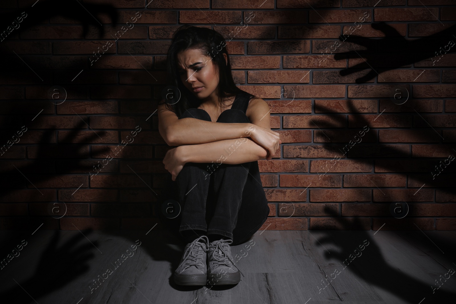 Image of Paranoid individual. Scared woman sitting near brick wall and having delusion as hands reaching for her