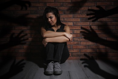 Paranoid individual. Scared woman sitting near brick wall and having delusion as hands reaching for her