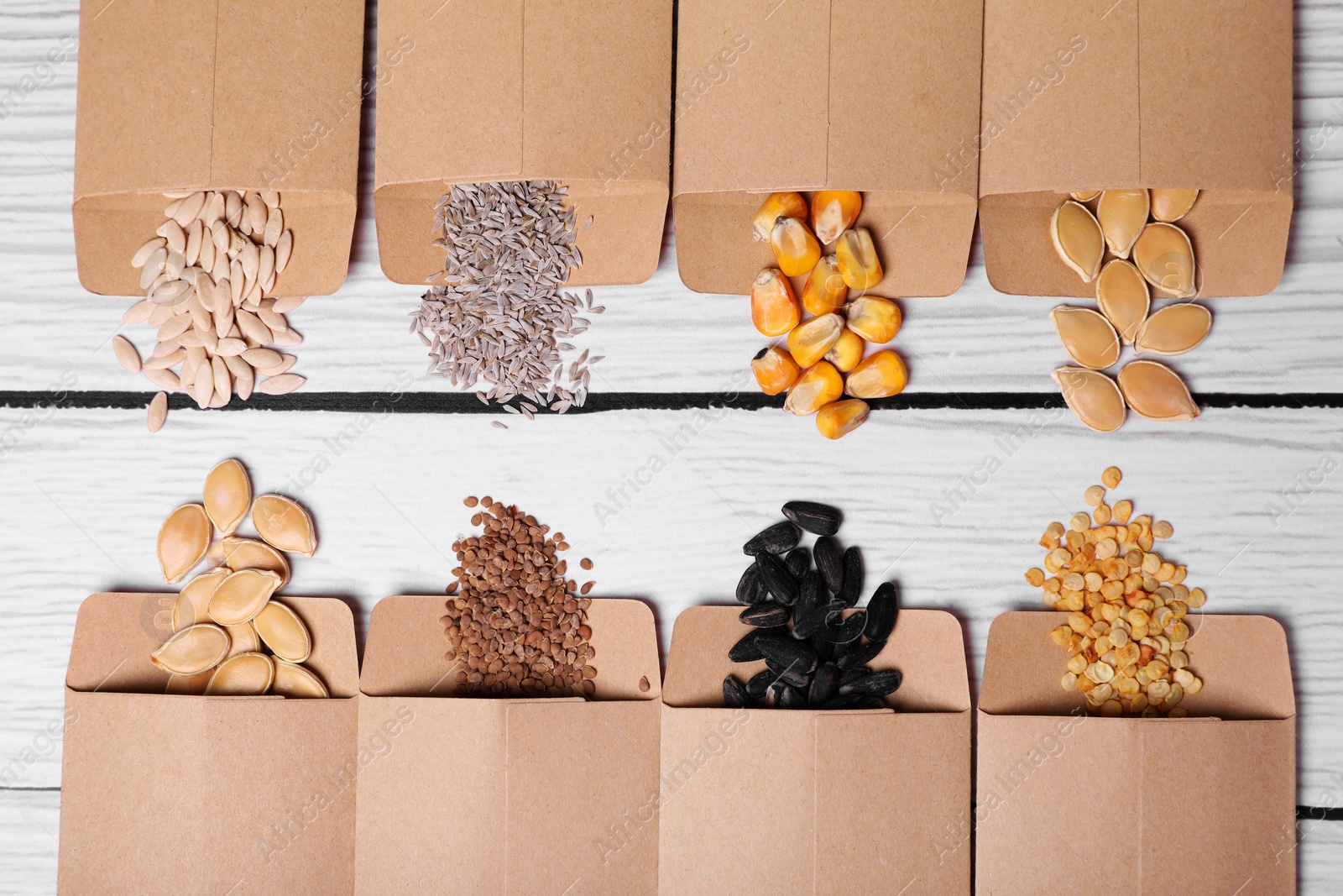 Photo of Many different vegetable seeds on white wooden table, flat lay