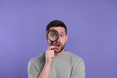 Surprised man looking through magnifier glass on violet background