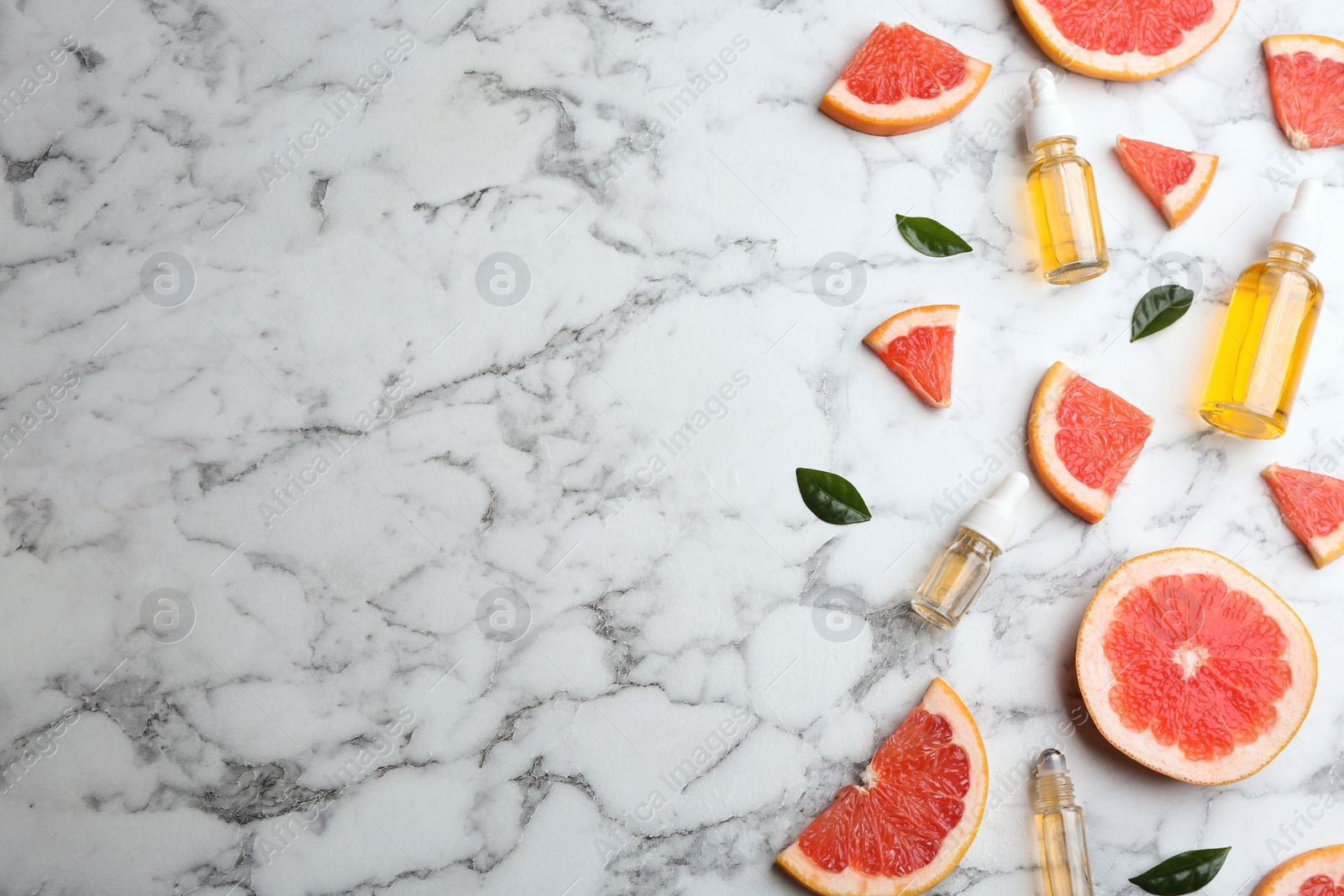 Photo of Flat lay composition with grapefruit slices and bottles of essential oil on marble background, space for text