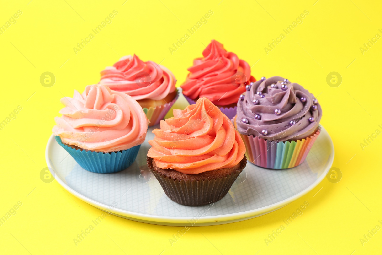 Photo of Delicious cupcakes with bright cream on yellow background