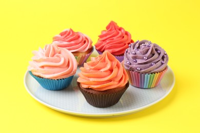 Delicious cupcakes with bright cream on yellow background