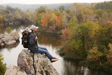 Photo of Hiker with travel backpack sitting on steep cliff near mountain river