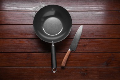 Empty iron wok and knife on wooden table, flat lay
