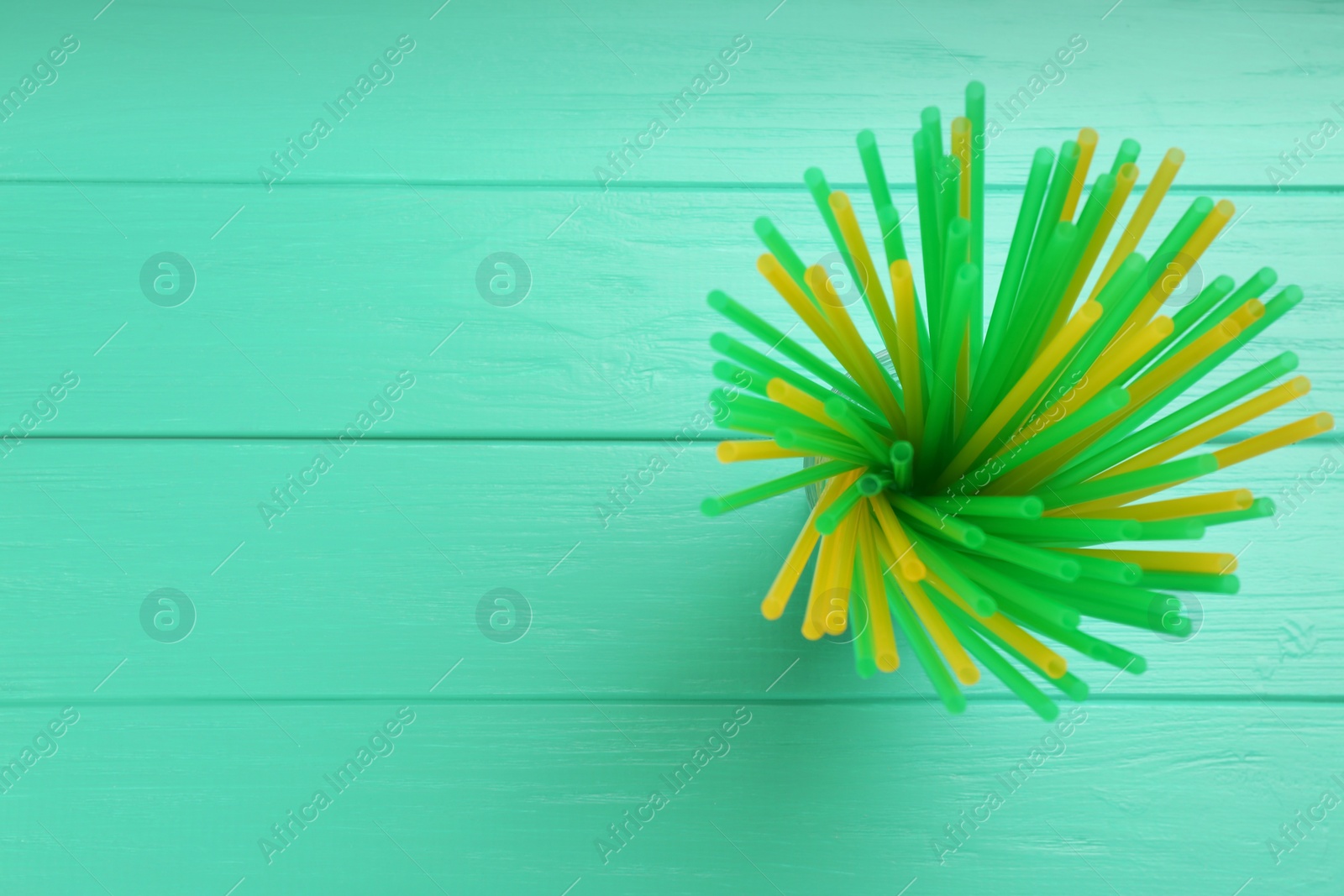Photo of Colorful plastic drinking straws on turquoise wooden table, top view. Space for text