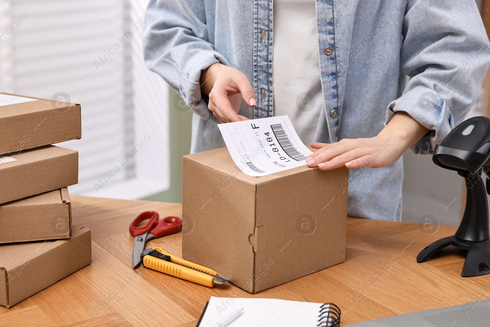 Photo of Parcel packing. Post office worker sticking barcode on box at wooden table indoors, closeup