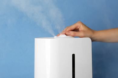 Photo of Woman using modern air humidifier on light blue background, closeup