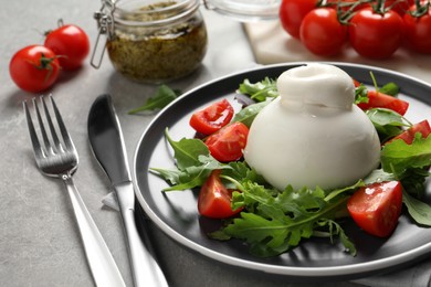 Photo of Delicious burrata salad with tomatoes and arugula served on grey table