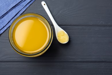 Glass jar and spoon of Ghee butter on grey wooden table, flat lay. Space for text