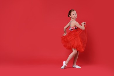 Photo of Cute little girl dancing on red background, space for text