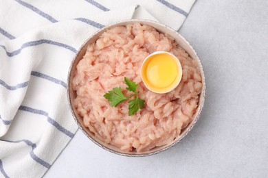 Fresh raw minced meat, parsley and egg in bowl on light grey table, top view