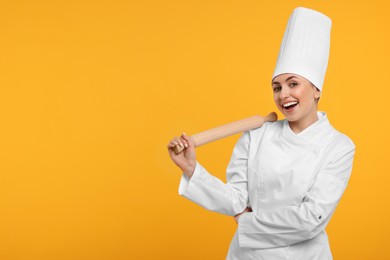 Photo of Happy professional confectioner in uniform holding rolling pin on yellow background. Space for text