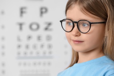 Photo of Little girl with glasses against vision test chart, closeup