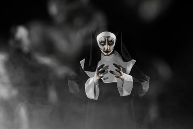 Photo of Portrait of scary devilish nun and smoke on black background, space for text. Halloween party look