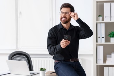 Photo of Smiling man with smartphone in office. Space for text