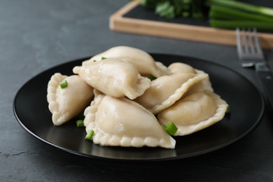 Plate of tasty dumplings served with green onion on table