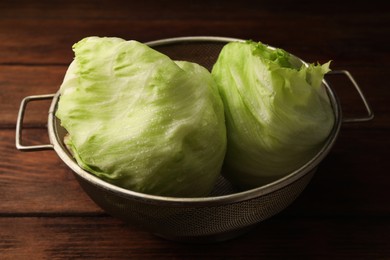 Colander with fresh green wet iceberg lettuce heads on wooden table, closeup