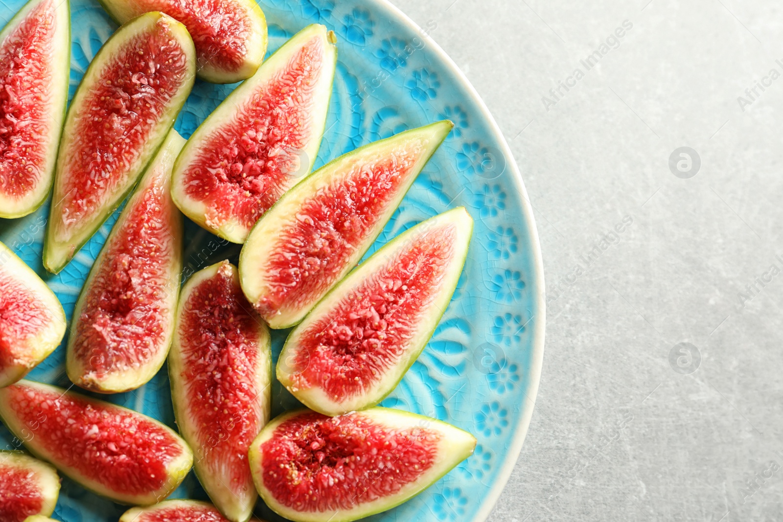 Photo of Plate with fresh ripe fig slices on gray background, top view. Space for text