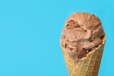 Photo of Delicious chocolate ice cream in waffle cone on light blue background, closeup. Space for text