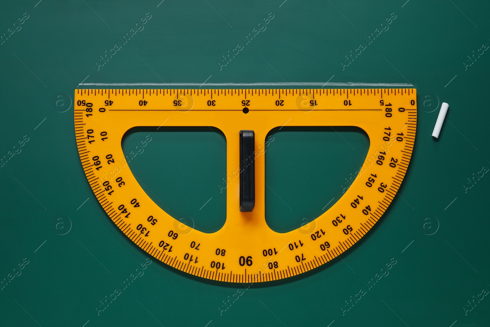 Photo of Yellow protractor and chalk on green chalkboard, flat lay