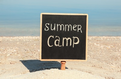 Photo of Small chalkboard with text SUMMER CAMP on beach near river