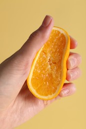 Woman squeezing juicy orange on beige background, closeup
