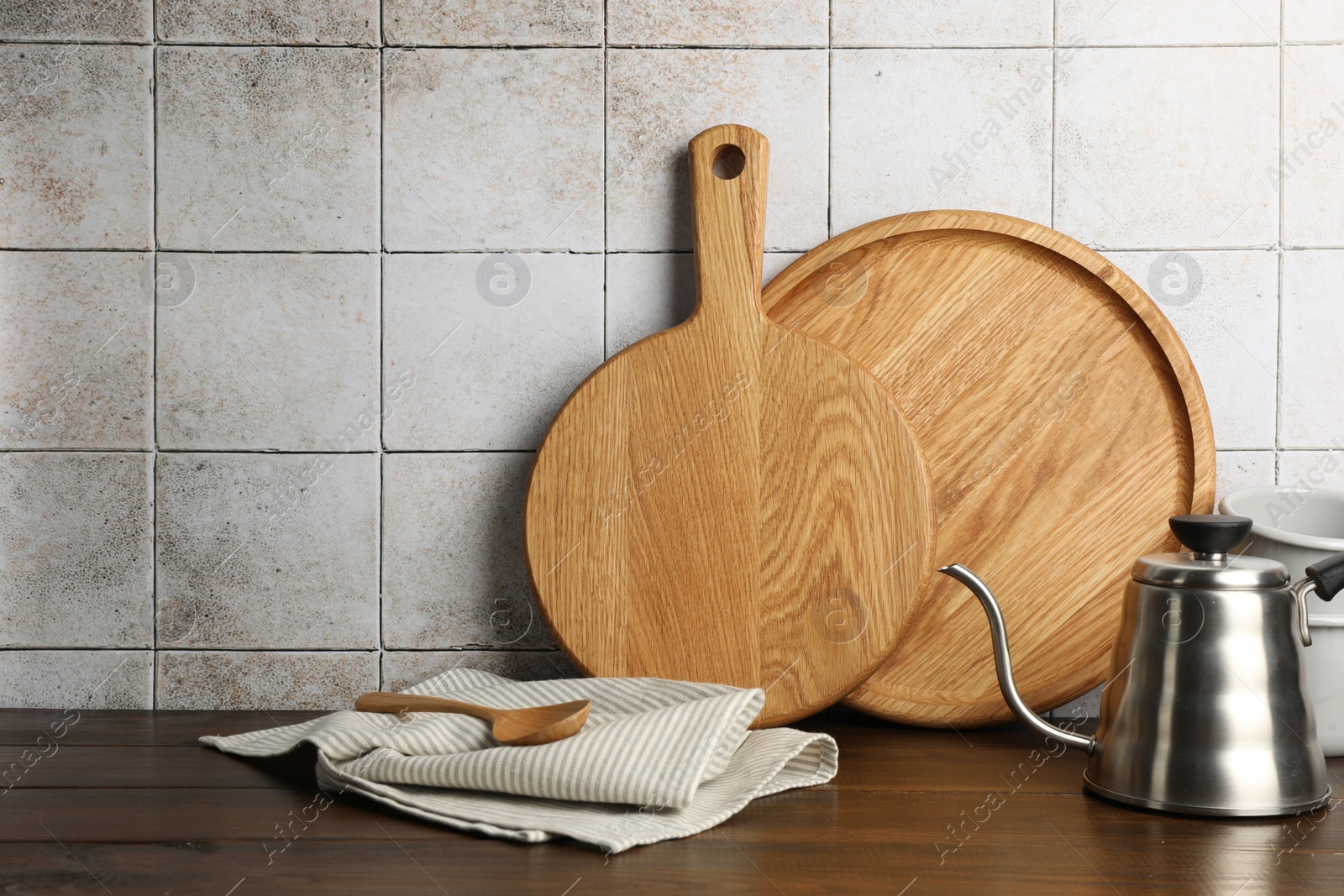 Photo of Wooden cutting boards, kettle and towel on table near tiled wall. Space for text