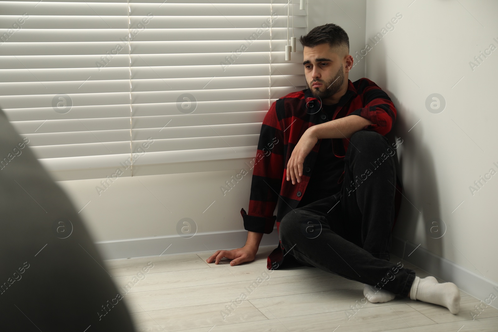 Photo of Sad man sitting on floor at home. Space for text