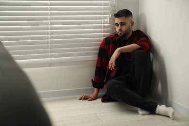 Photo of Sad man sitting on floor at home. Space for text