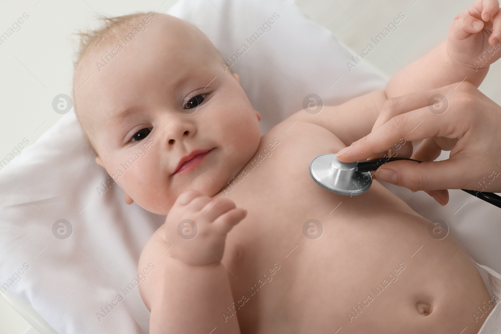 Photo of Pediatrician examining cute little baby with stethoscope in clinic, closeup