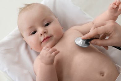 Photo of Pediatrician examining cute little baby with stethoscope in clinic, closeup