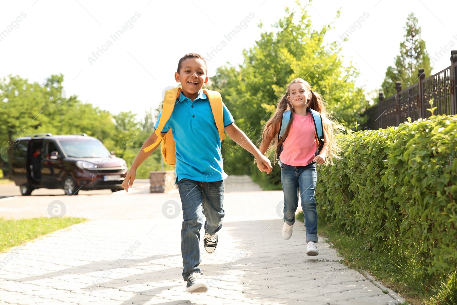 Photo of Cute little children with backpacks running outdoors. Elementary school