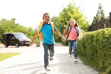 Photo of Cute little children with backpacks running outdoors. Elementary school