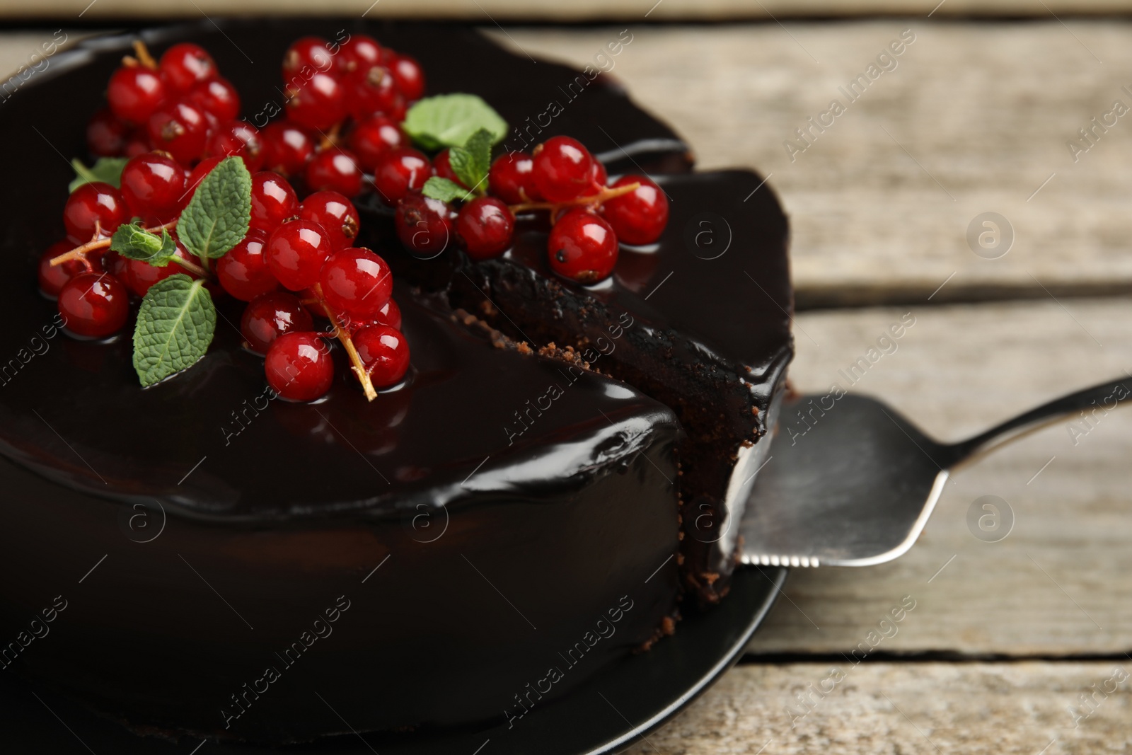 Photo of Tasty homemade chocolate cake with berries and mint on wooden table, closeup